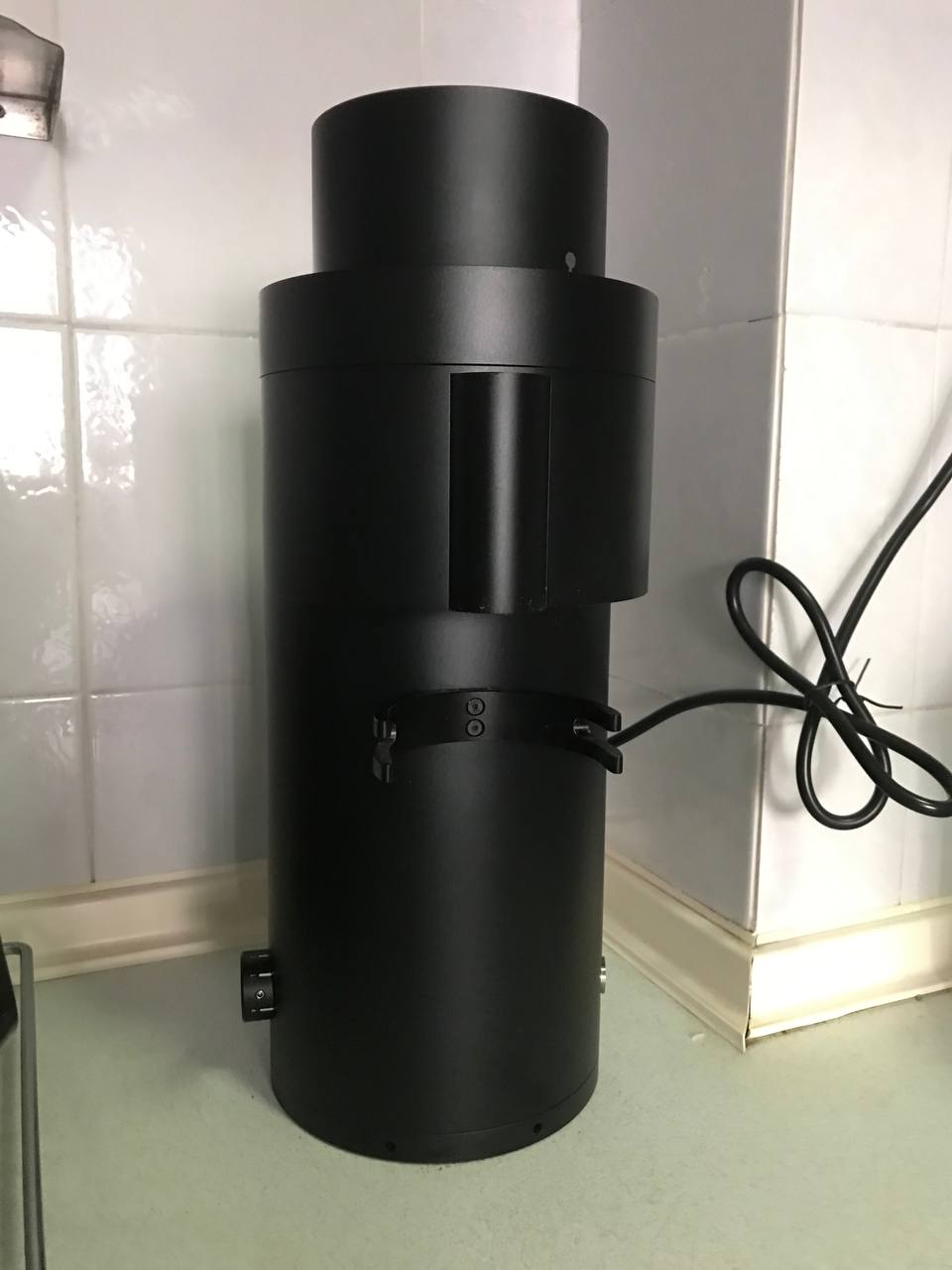 The P100 anodized in black has a cylindrical body with a smaller bean intake funnel at the top. Prongs of the integrated portafilter fork protrude from the front, near the exit chute where ground coffee is dispensed.