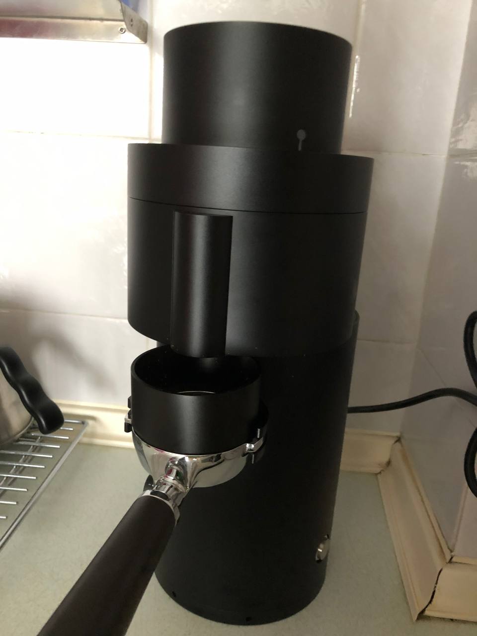 The P100 with an empty portafilter mounted onto the integrated portafilter fork. A dosing funnel placed on top of the portafilter keeps ground coffee from flying out from the gap between the exit chute and the portafilter basket.