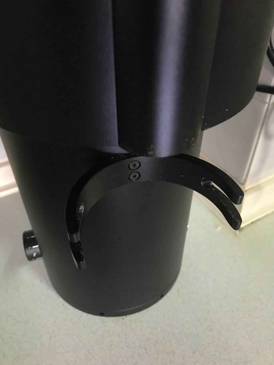 The integrated portafilter fork at the front of the P100 sits below the exit chute. The fork consists of 2 pairs of metal prongs for the ears of a portafilter to rest between.