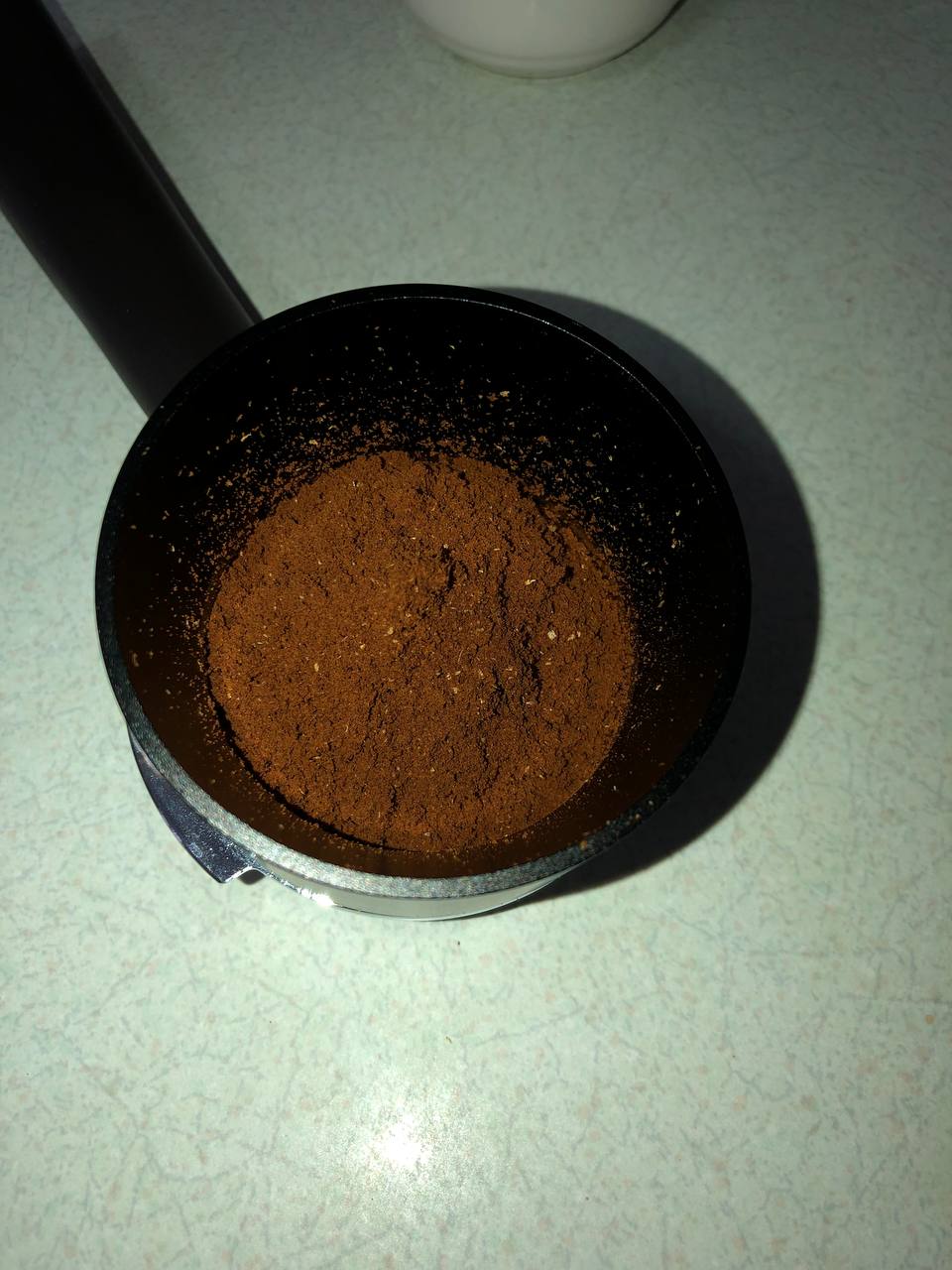 A portafilter with a dosing funnel holds fluffy finely ground coffee from the P100. There is a mound at the center of the ground coffee.